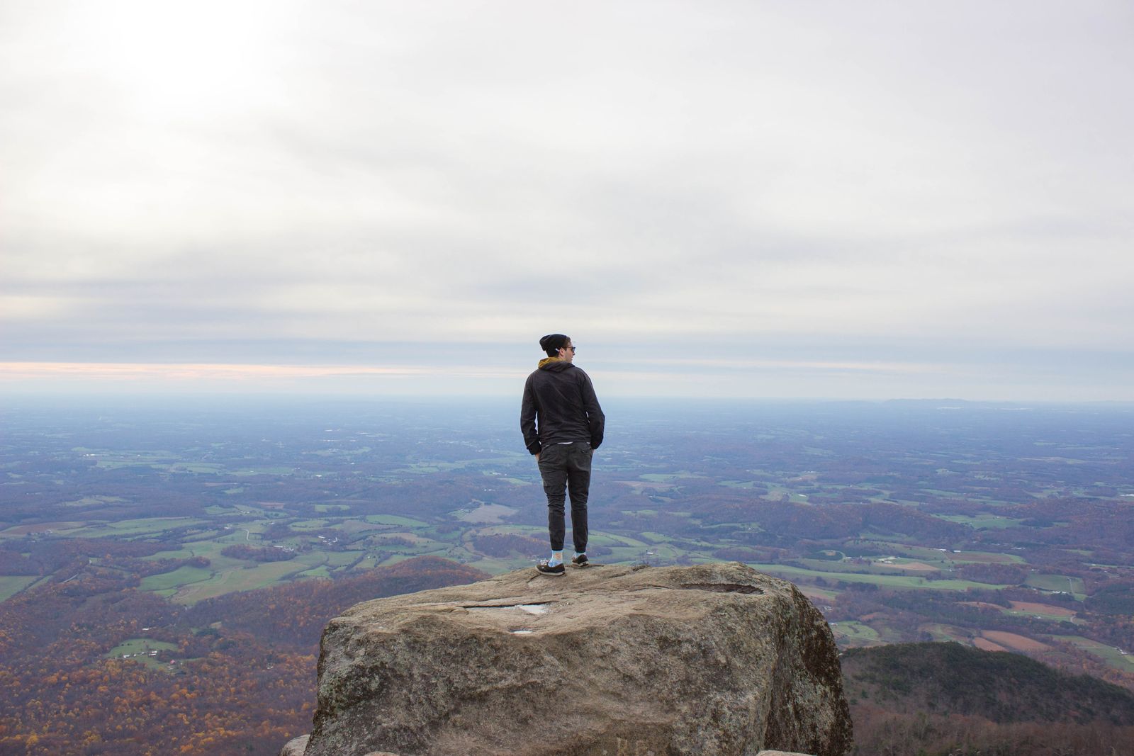 A hiker standing on a rocky summit above a wide valley under an overcast sky