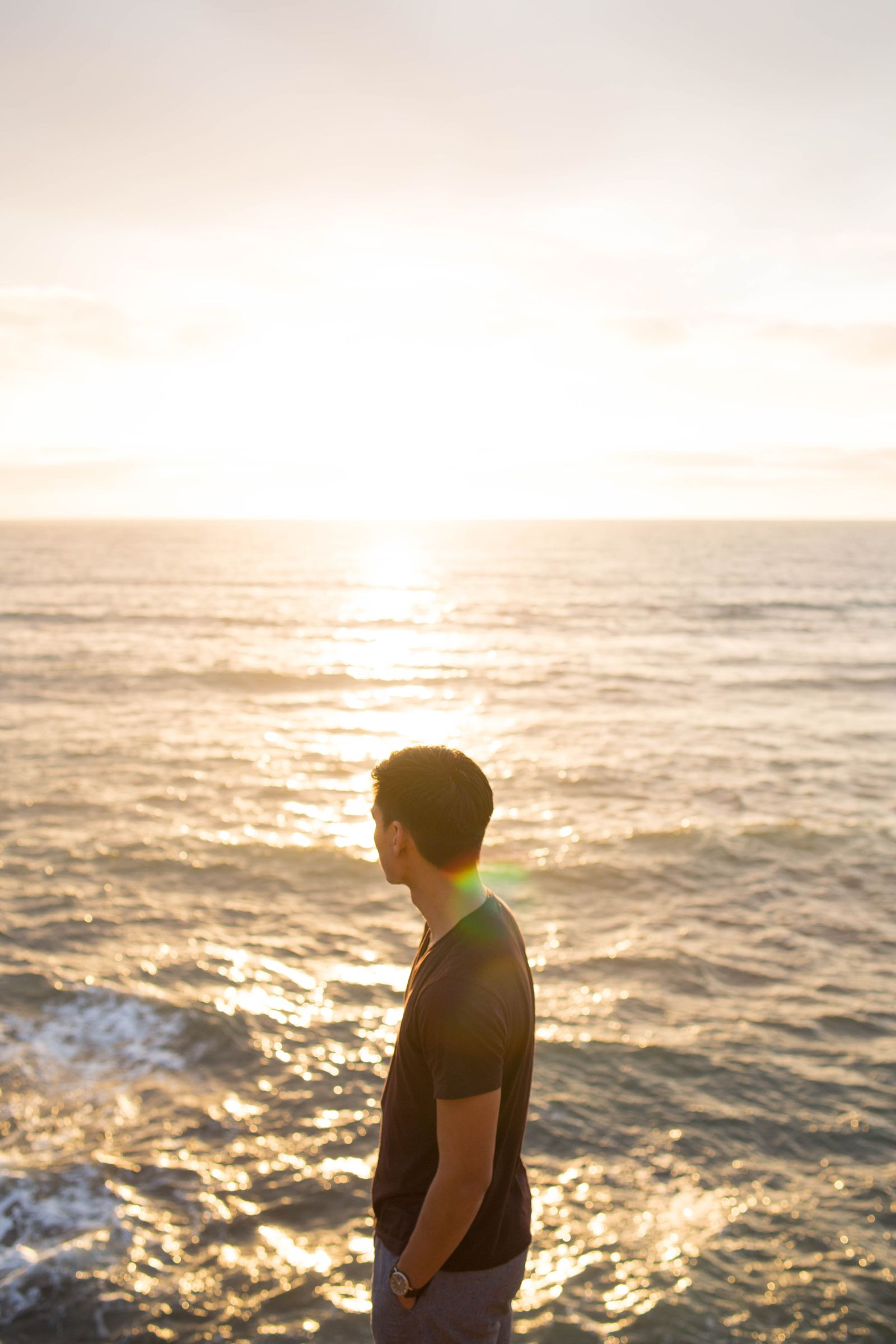 A man watching the sun set over the ocean from a rocky shore