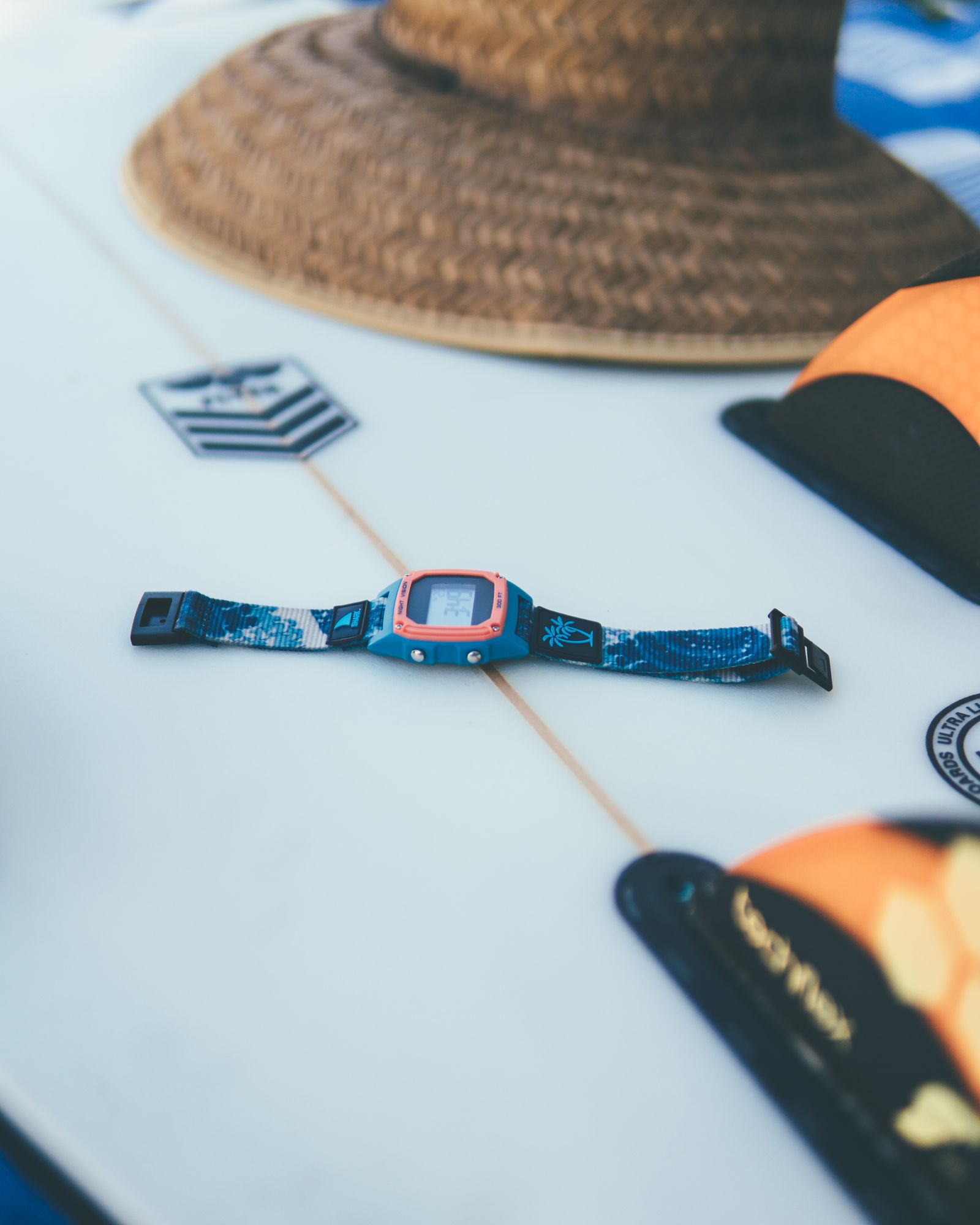 A Freestyle watch lying on a white surfboard next to a straw hat and fins