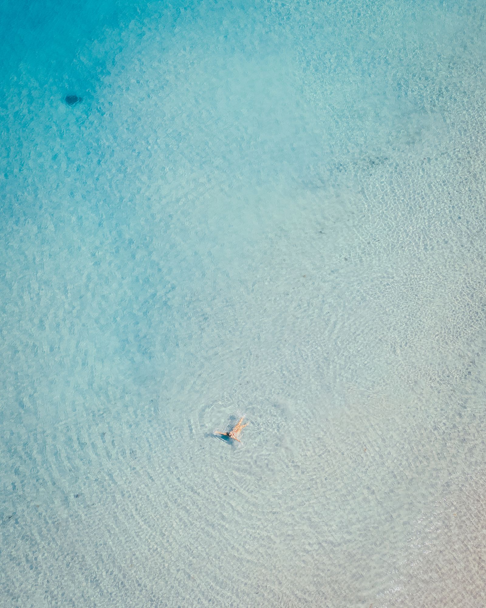 A lone swimmer in clear, pale turquoise water off Deerfield Beach