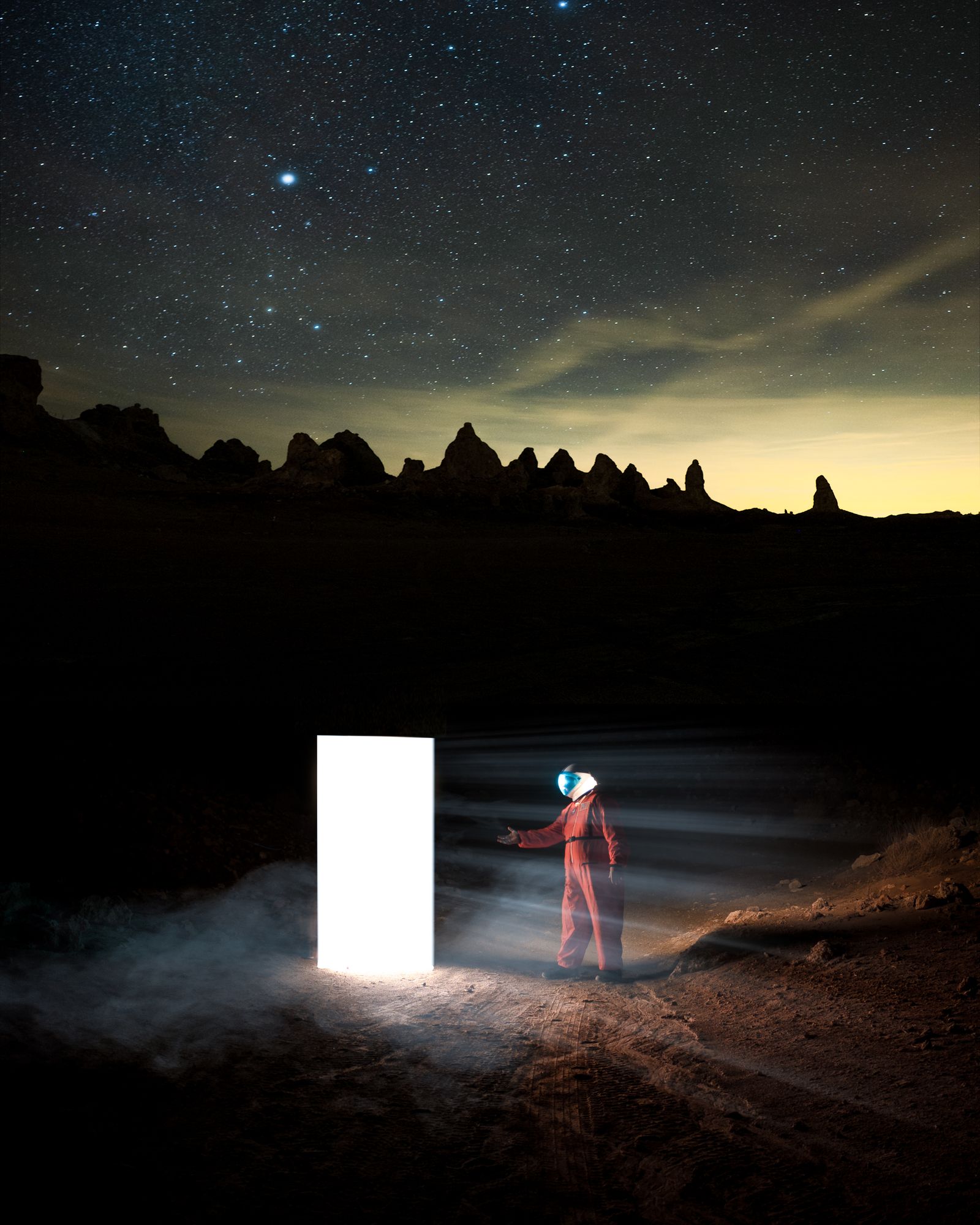 A figure in a spacesuit reaching toward a glowing white door in a dark desert under the stars