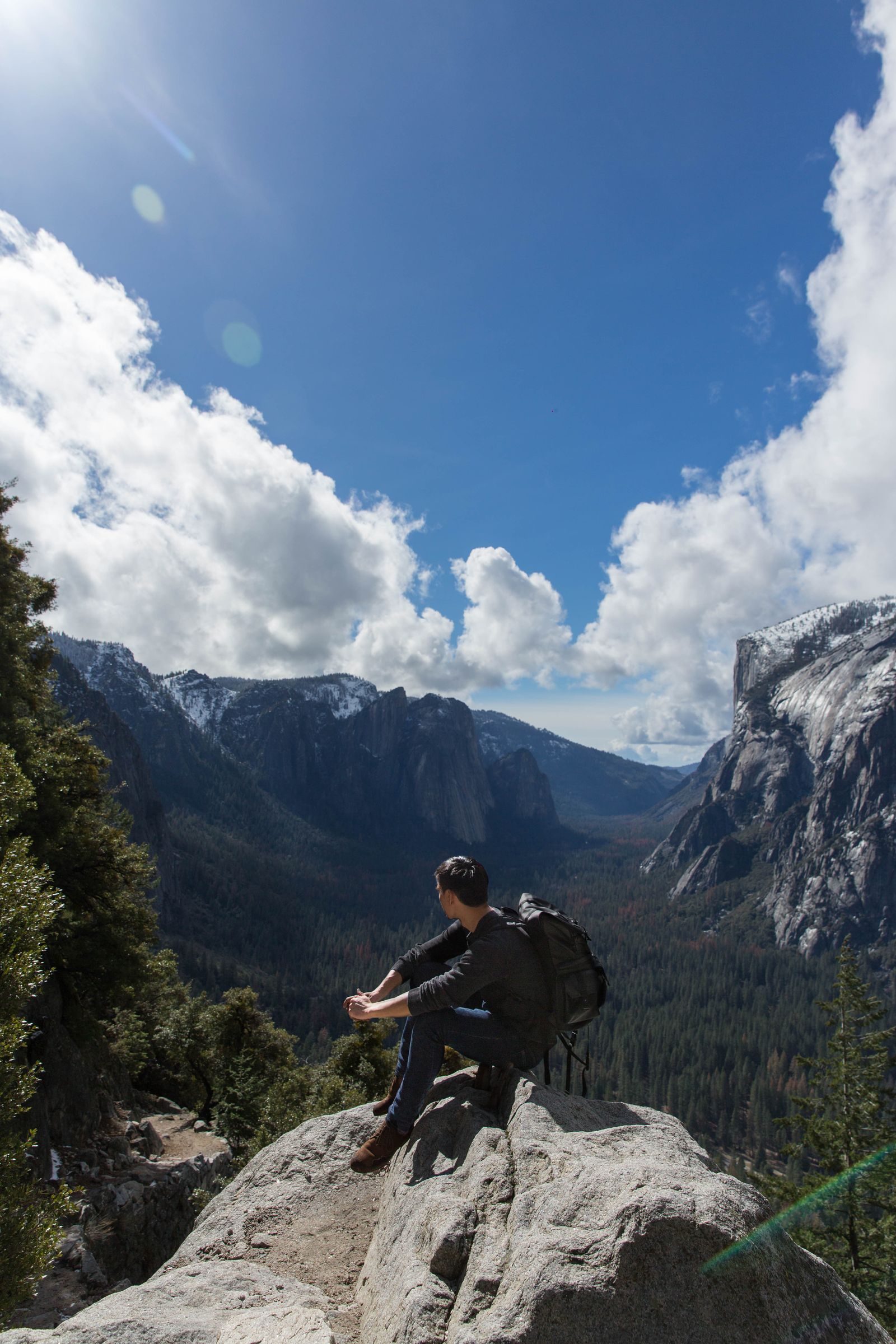 A hiker sitting on a granite ledge above Yosemite Valley under a bright sky