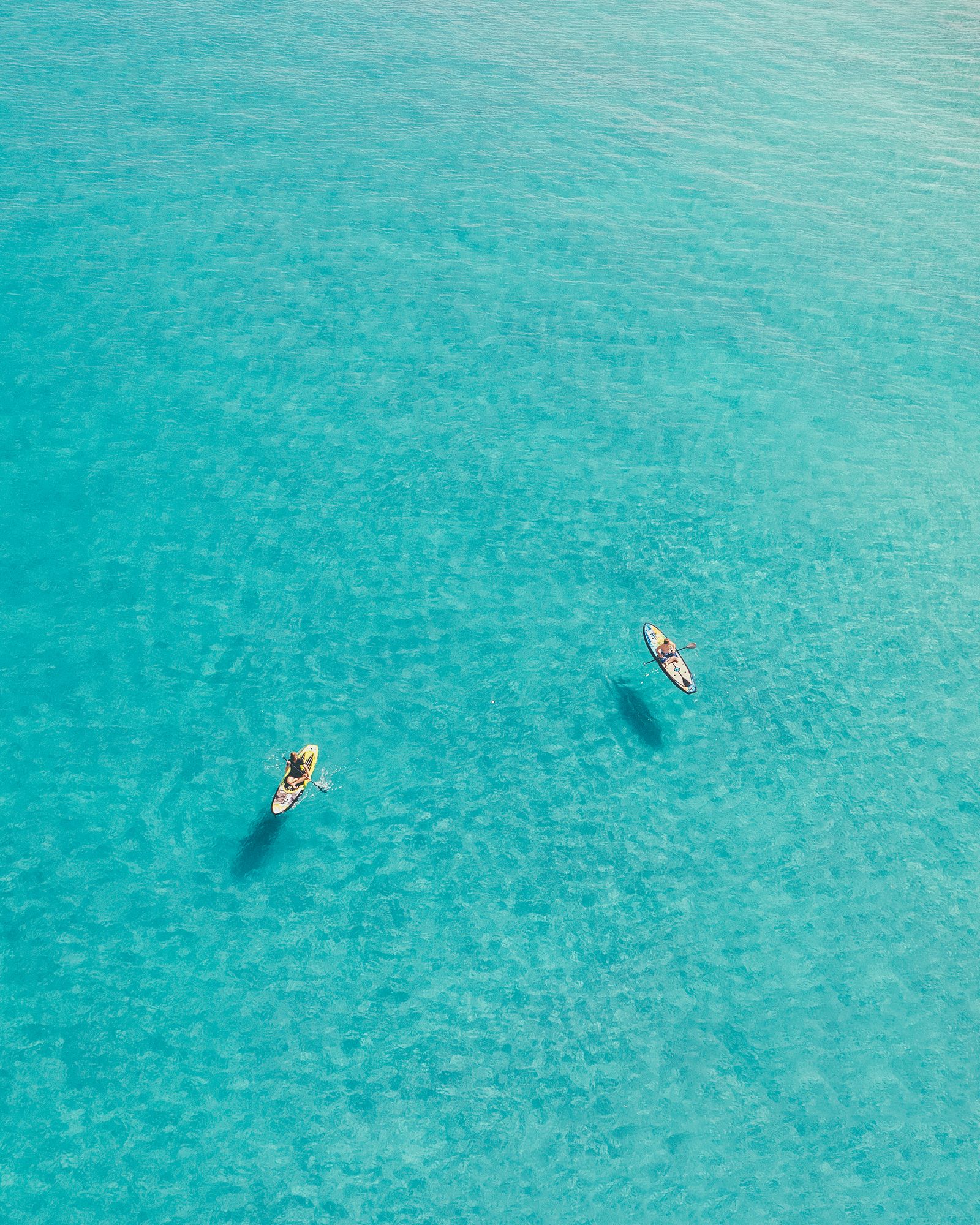 Two paddleboarders far apart on calm turquoise water off Deerfield Beach