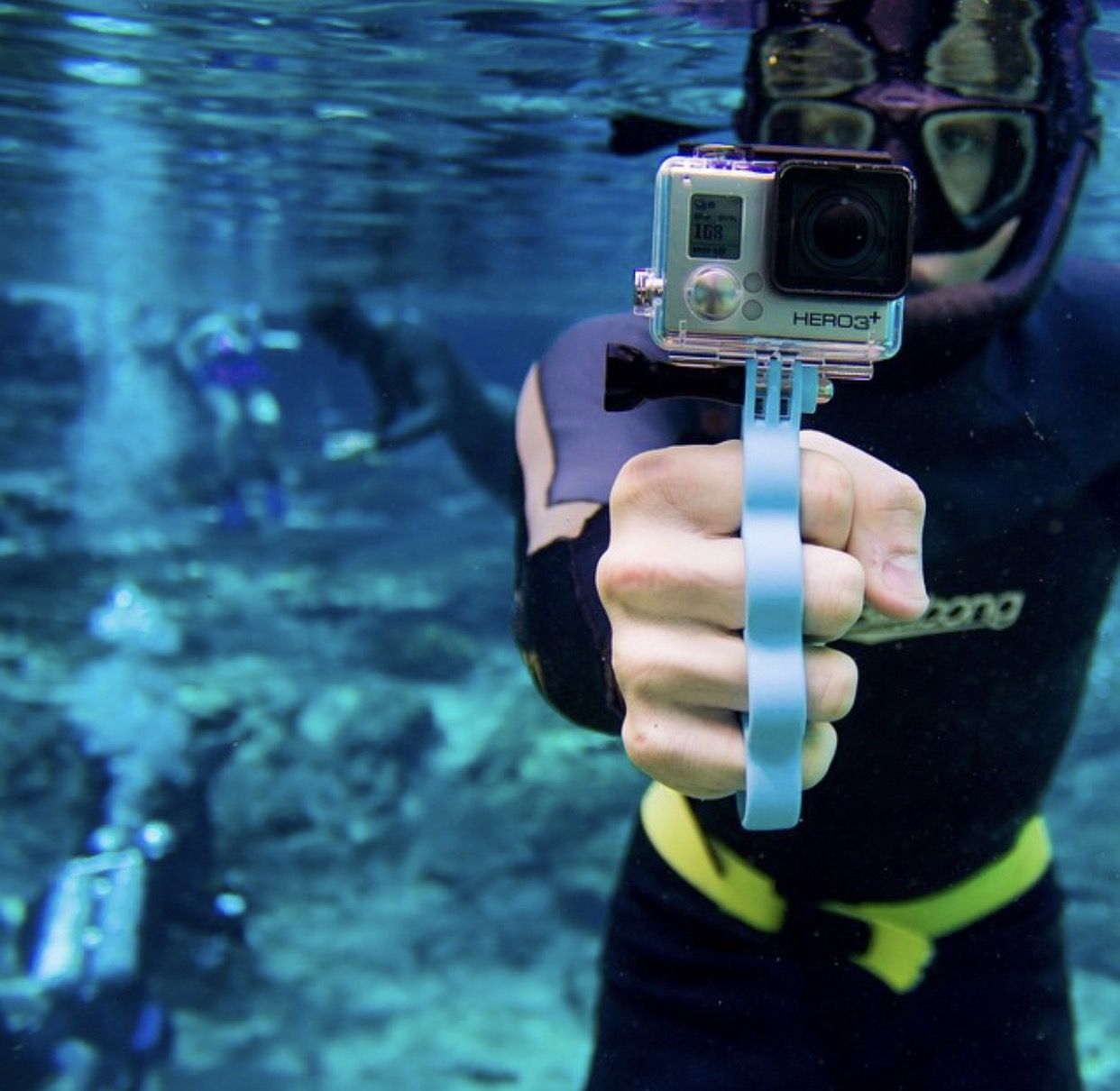 A snorkeler holding a GoPro on a floating hand grip toward the camera underwater