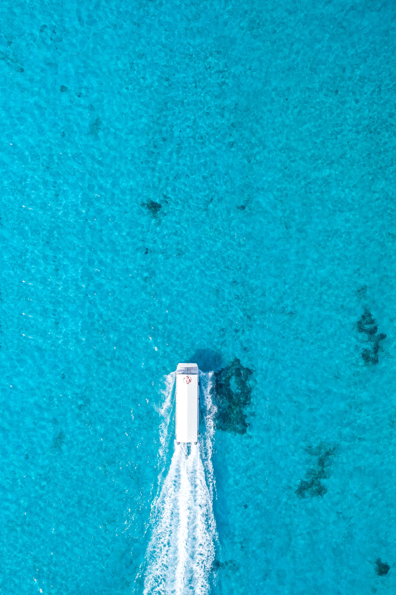 A boat's white wake cutting straight through bright blue water, from directly above