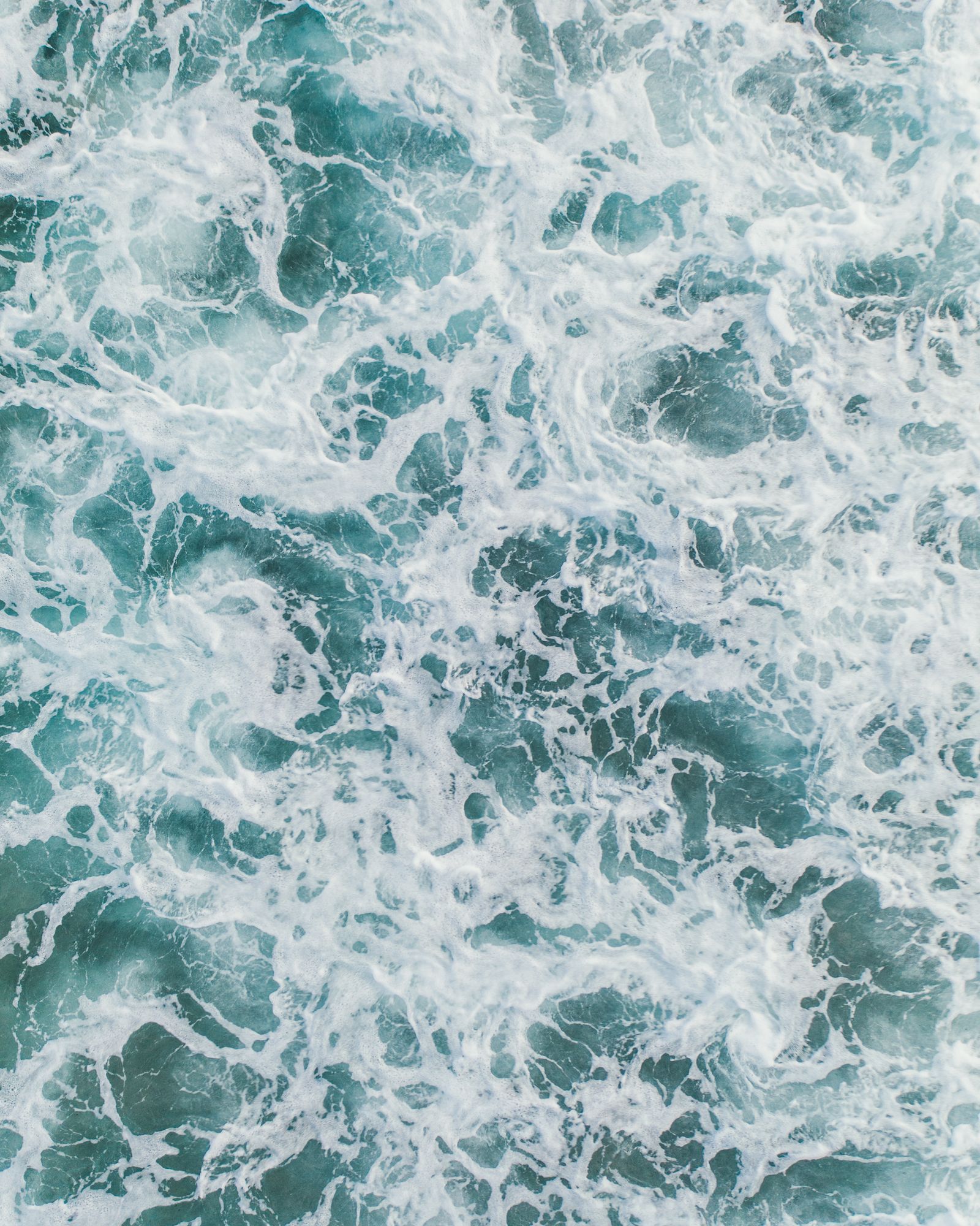 Swirling whitewater and dark green sea seen from directly above